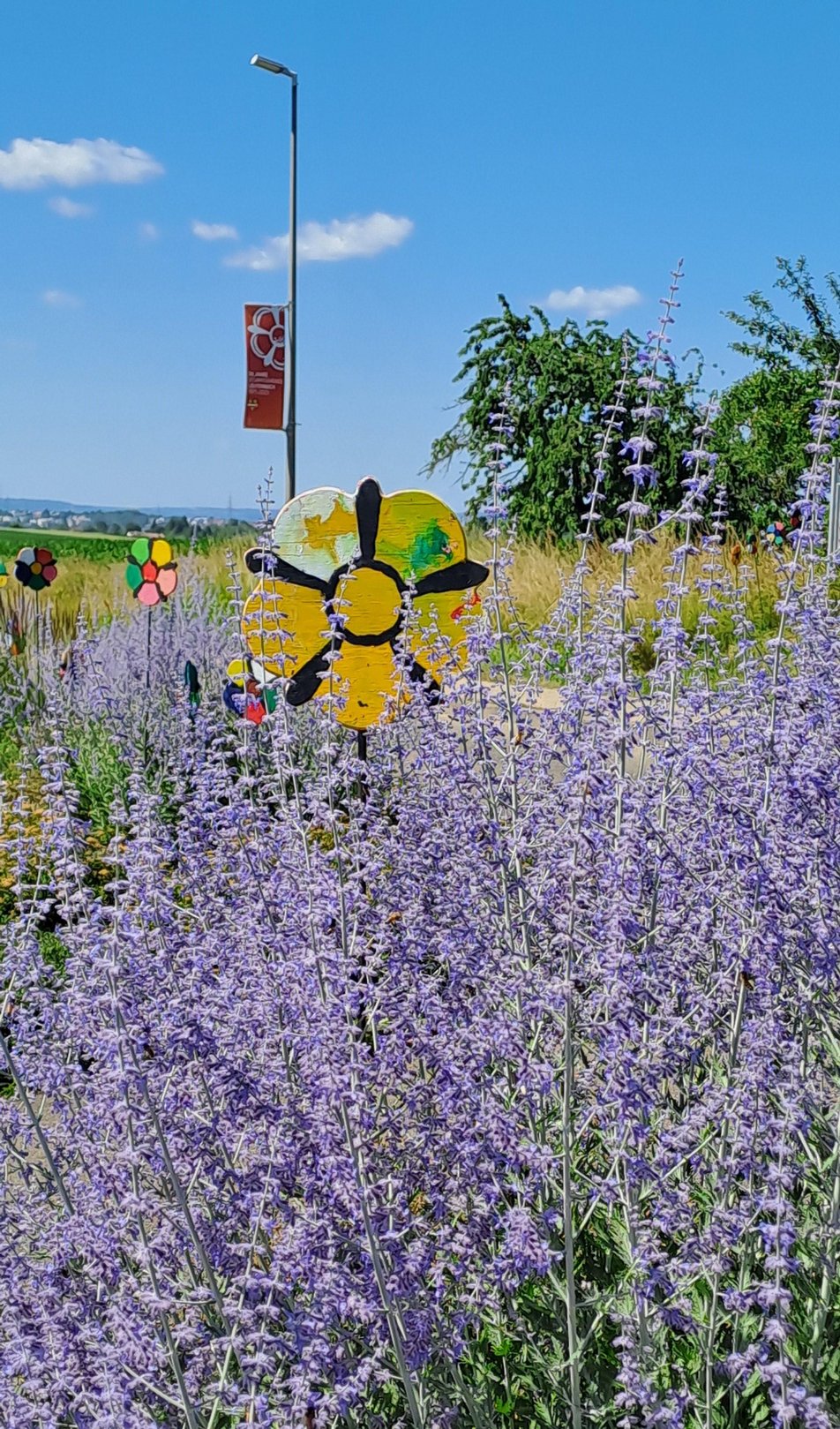 Holzblume stehend in lila Blumen. Im Hintergrund Jubiläumsflagge